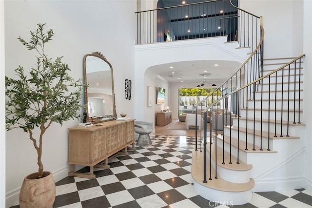 entryway featuring stairway, tile patterned floors, arched walkways, a towering ceiling, and baseboards