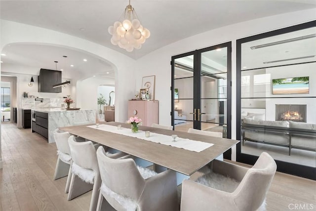 dining space featuring arched walkways, light wood finished floors, and recessed lighting