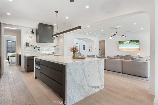 kitchen featuring arched walkways, a center island with sink, light wood-type flooring, modern cabinets, and pendant lighting