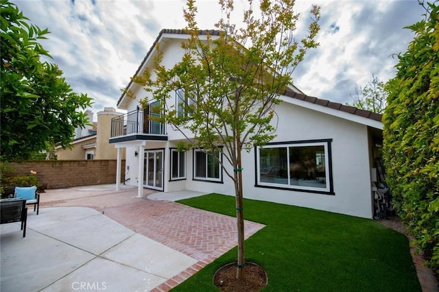 back of property with fence, a balcony, a patio, stucco siding, and a yard