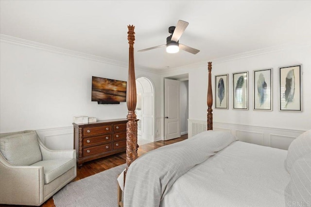 bedroom with crown molding, a decorative wall, ceiling fan, wood finished floors, and wainscoting