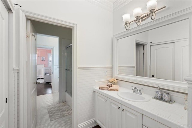 ensuite bathroom featuring crown molding, vanity, wainscoting, and a shower with door