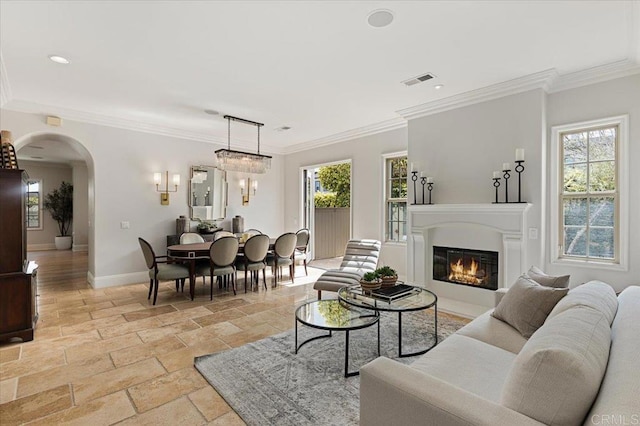 living area featuring arched walkways, stone tile floors, ornamental molding, visible vents, and baseboards
