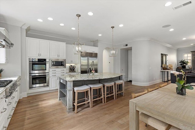 kitchen with visible vents, built in appliances, an island with sink, recessed lighting, and a breakfast bar area
