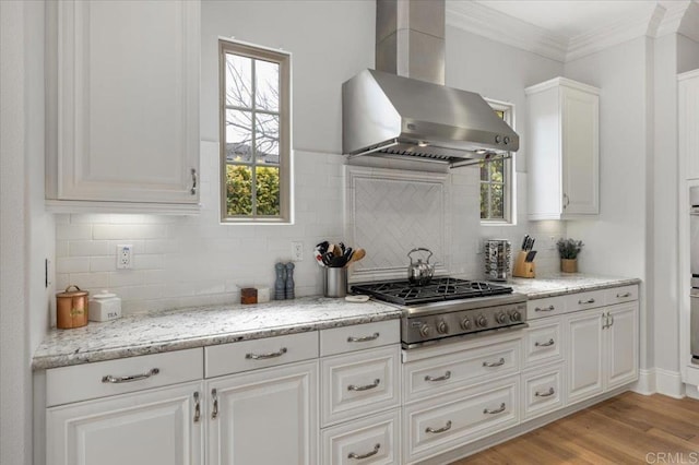 kitchen with ornamental molding, wall chimney range hood, white cabinetry, backsplash, and stainless steel gas cooktop