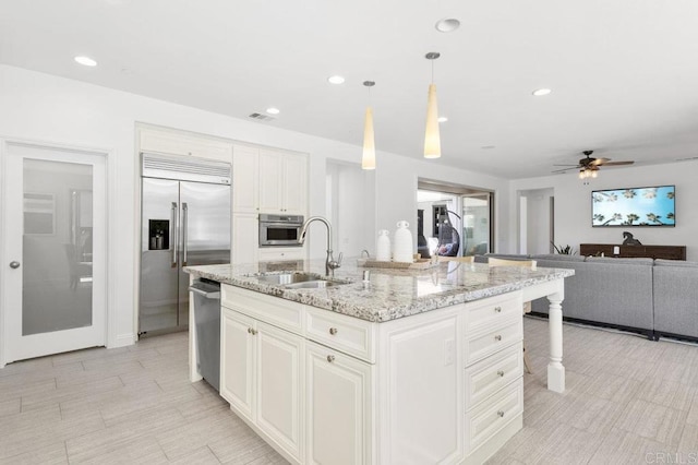 kitchen featuring visible vents, a ceiling fan, a sink, light stone countertops, and appliances with stainless steel finishes