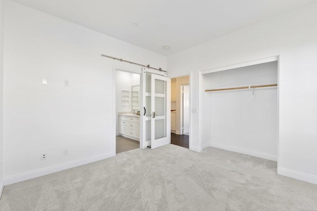 unfurnished bedroom featuring a barn door, ensuite bathroom, a closet, carpet, and baseboards