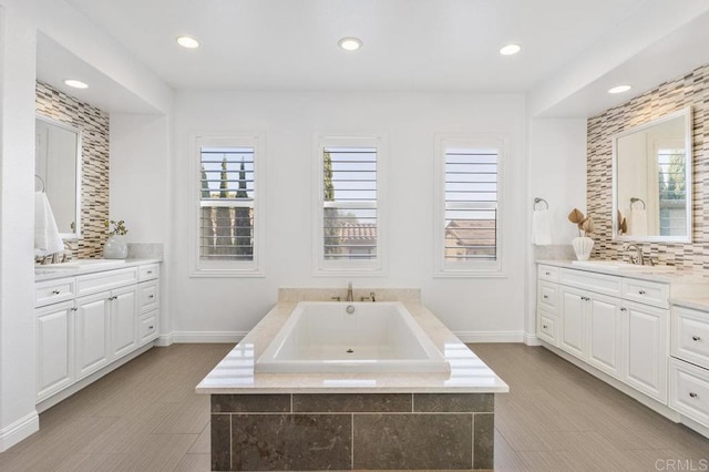 full bath featuring two vanities, a sink, baseboards, decorative backsplash, and a garden tub