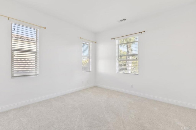 empty room featuring baseboards, visible vents, and light colored carpet