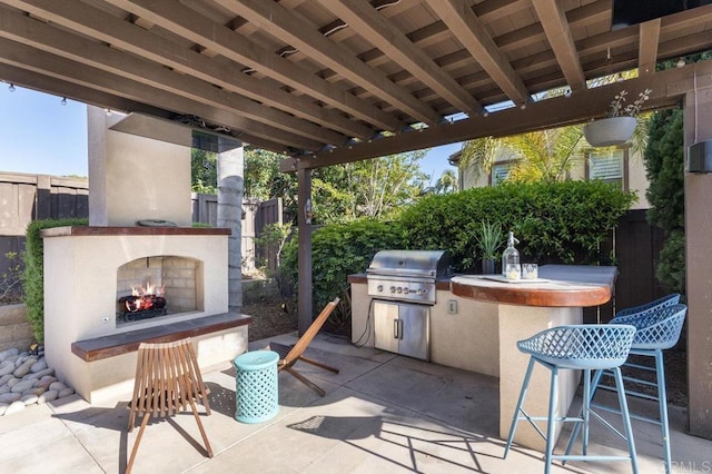 view of patio with a warm lit fireplace, fence, a bar, and area for grilling