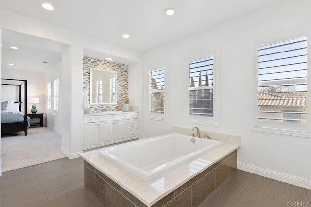 ensuite bathroom featuring recessed lighting, vanity, connected bathroom, baseboards, and a garden tub
