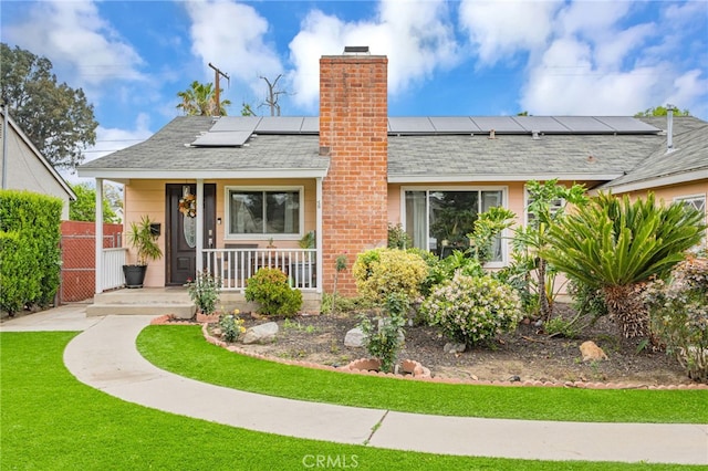 view of front of property with covered porch, a front yard, solar panels, a chimney, and a shingled roof