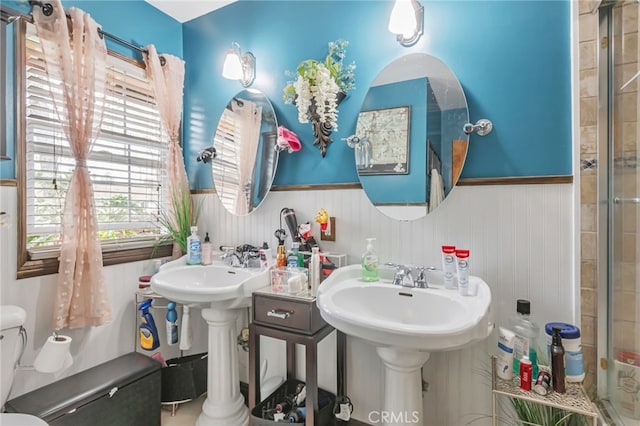 full bathroom with toilet, tiled shower, and a wainscoted wall