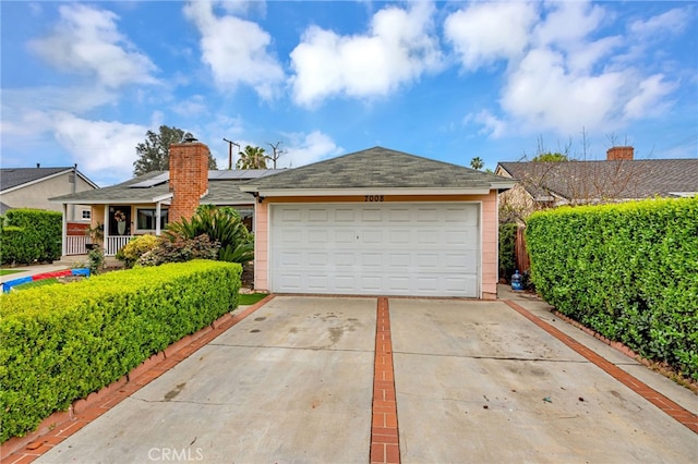 view of front of home with an attached garage, roof mounted solar panels, concrete driveway, and a chimney