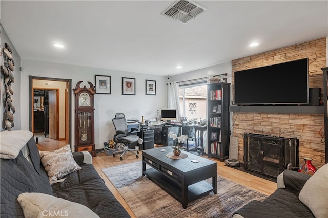 living area with wood finished floors, a stone fireplace, visible vents, and recessed lighting