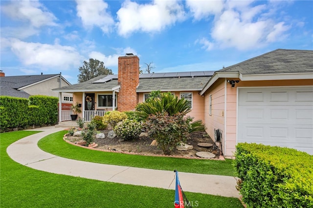 single story home with covered porch, a front yard, solar panels, an attached garage, and a chimney