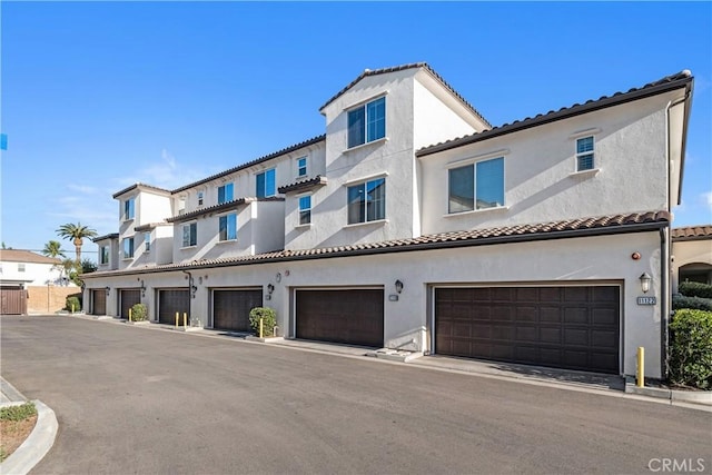 multi unit property with an attached garage, a tiled roof, and stucco siding