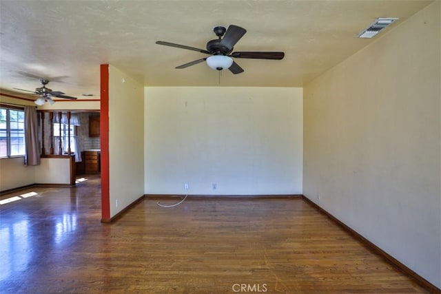 empty room featuring a ceiling fan, visible vents, wood finished floors, and baseboards