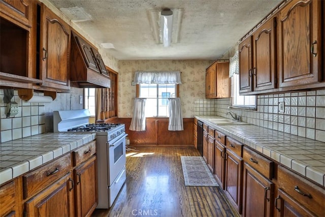 kitchen featuring dark wood-type flooring, a sink, tile counters, and gas range gas stove
