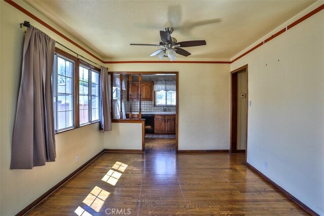 spare room with crown molding, dark wood-style floors, a ceiling fan, and baseboards