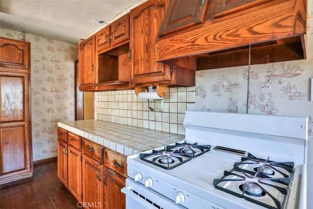 kitchen with white gas stove, tile countertops, premium range hood, wallpapered walls, and dark wood finished floors