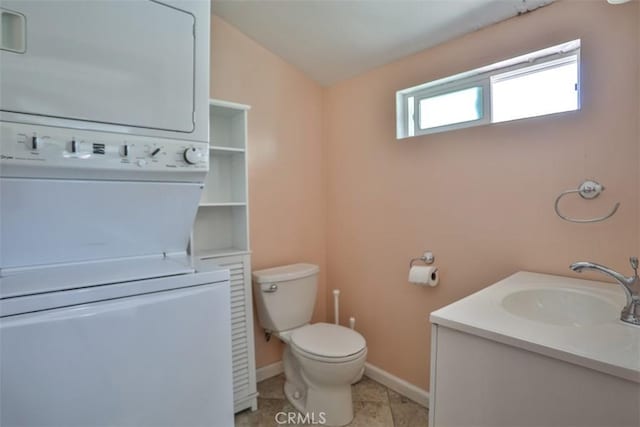 bathroom with stacked washer and clothes dryer, baseboards, toilet, vanity, and tile patterned flooring