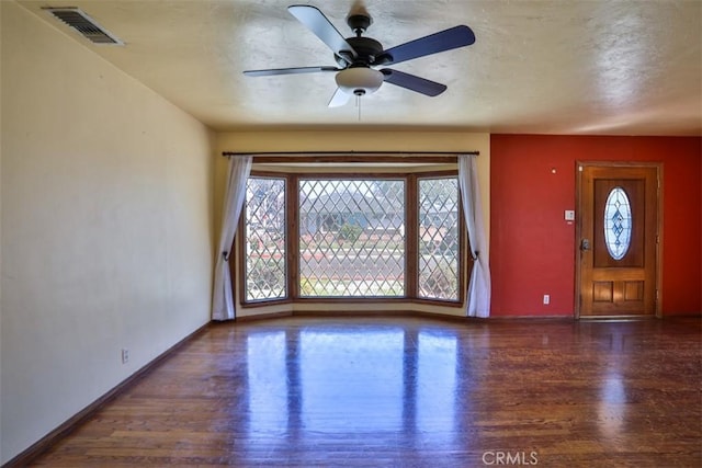 unfurnished living room featuring a wealth of natural light, visible vents, wood finished floors, and baseboards