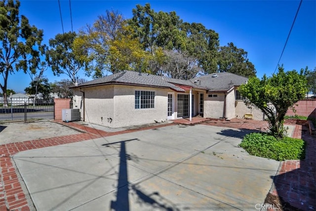 view of front of home featuring stucco siding, a gate, fence, a patio, and central AC