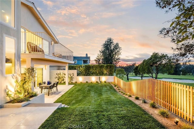 yard at dusk with a fenced backyard, a balcony, and a patio
