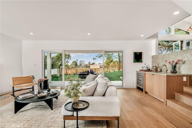 living room with wet bar, a healthy amount of sunlight, wine cooler, and light wood-style flooring