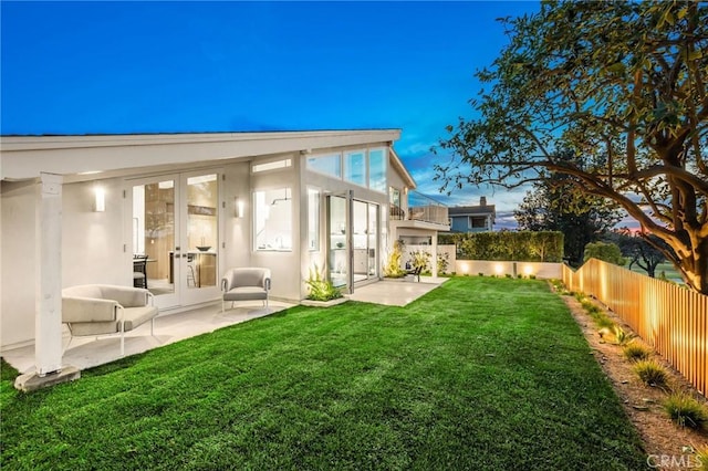 rear view of house featuring a fenced backyard, a yard, stucco siding, french doors, and a patio