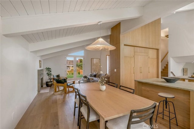 dining space with lofted ceiling with beams, light wood finished floors, stairs, and wood ceiling
