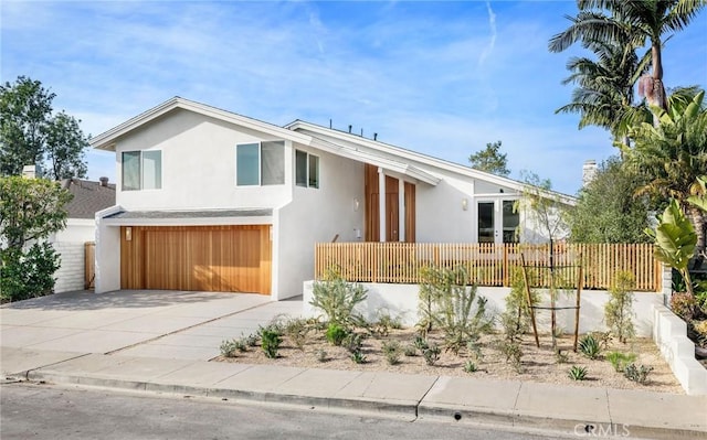 view of front facade with stucco siding, an attached garage, driveway, and fence private yard