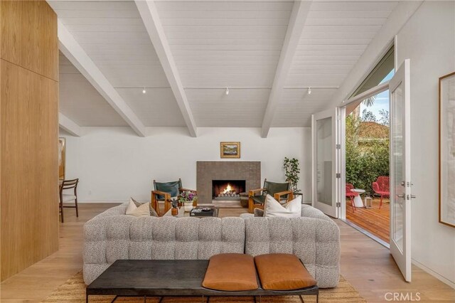 living area featuring a warm lit fireplace, light wood finished floors, wooden ceiling, and vaulted ceiling with beams