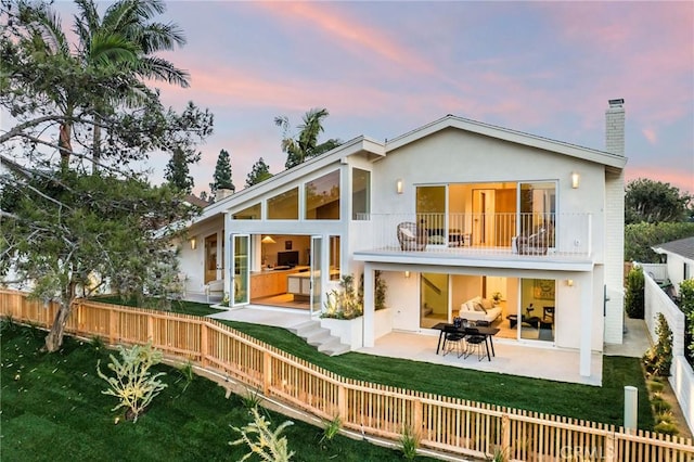 back of property with a chimney, a fenced backyard, a balcony, a patio, and a lawn