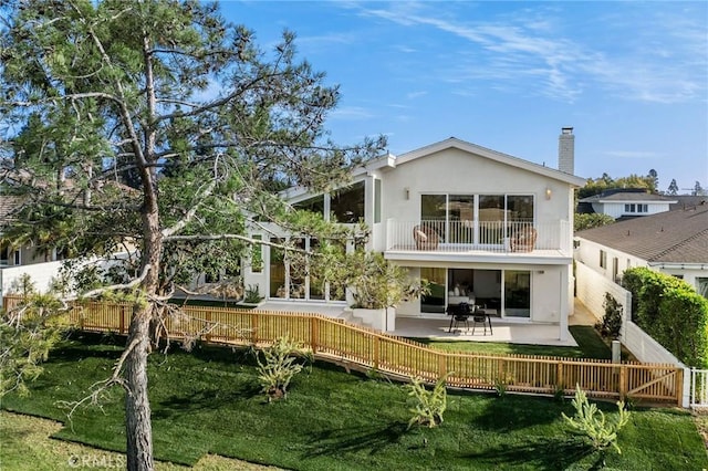 rear view of house featuring a chimney, a fenced backyard, a balcony, stucco siding, and a patio area