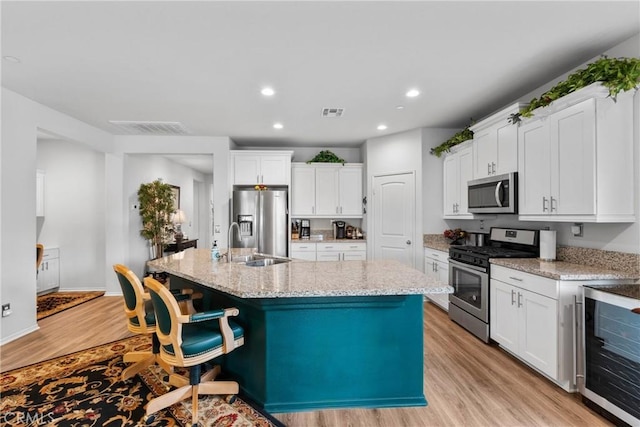 kitchen featuring a kitchen island with sink, white cabinets, a sink, and stainless steel appliances