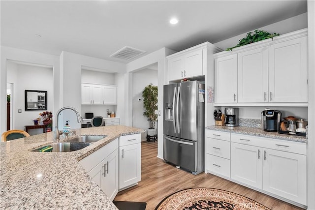 kitchen with white cabinets, visible vents, stainless steel fridge, a sink, and light wood-style floors