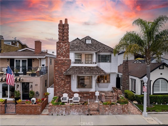 view of front facade featuring a gate, a chimney, fence private yard, and a balcony