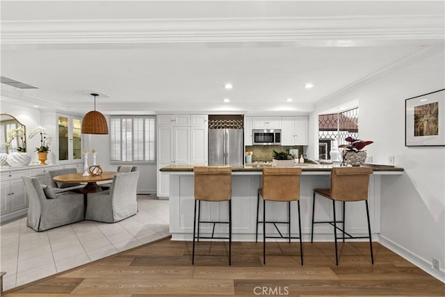 kitchen with a kitchen bar, white cabinets, a peninsula, ornamental molding, and stainless steel appliances