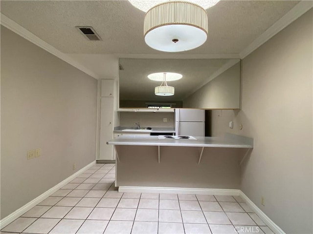 kitchen featuring a textured ceiling, visible vents, a peninsula, a sink, and freestanding refrigerator