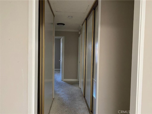 hallway with light carpet, baseboards, attic access, and ornamental molding