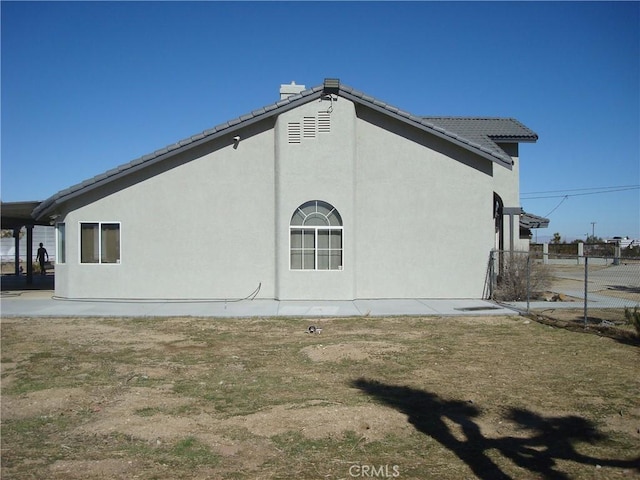 view of side of home featuring stucco siding, fence, and a tiled roof
