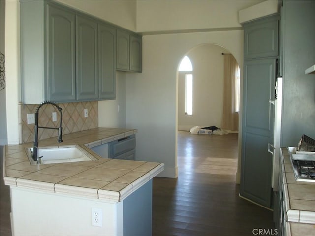 kitchen with dark wood finished floors, arched walkways, tasteful backsplash, tile countertops, and a sink