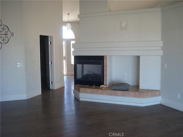 unfurnished living room featuring baseboards, a multi sided fireplace, and dark wood finished floors