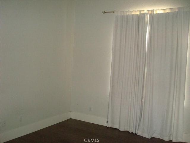 spare room featuring dark wood-style floors and baseboards