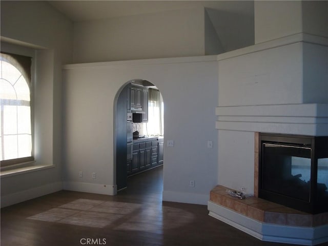 interior space featuring dark wood-style flooring, a tiled fireplace, arched walkways, and a healthy amount of sunlight
