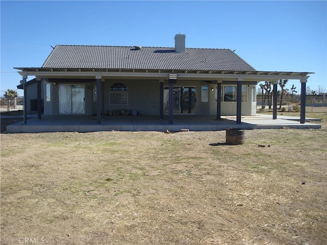 rear view of house featuring a chimney, stucco siding, a tiled roof, and a patio