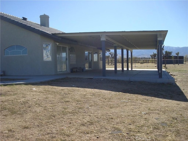 rear view of property featuring a chimney, stucco siding, a mountain view, and a patio area