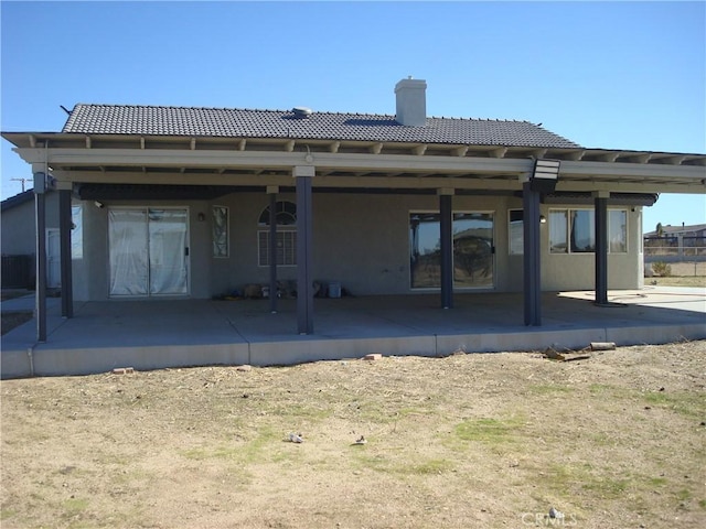 rear view of property featuring a tile roof, a patio, stucco siding, and a chimney